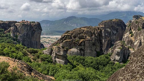 a rocky mountains with trees and a city in the background